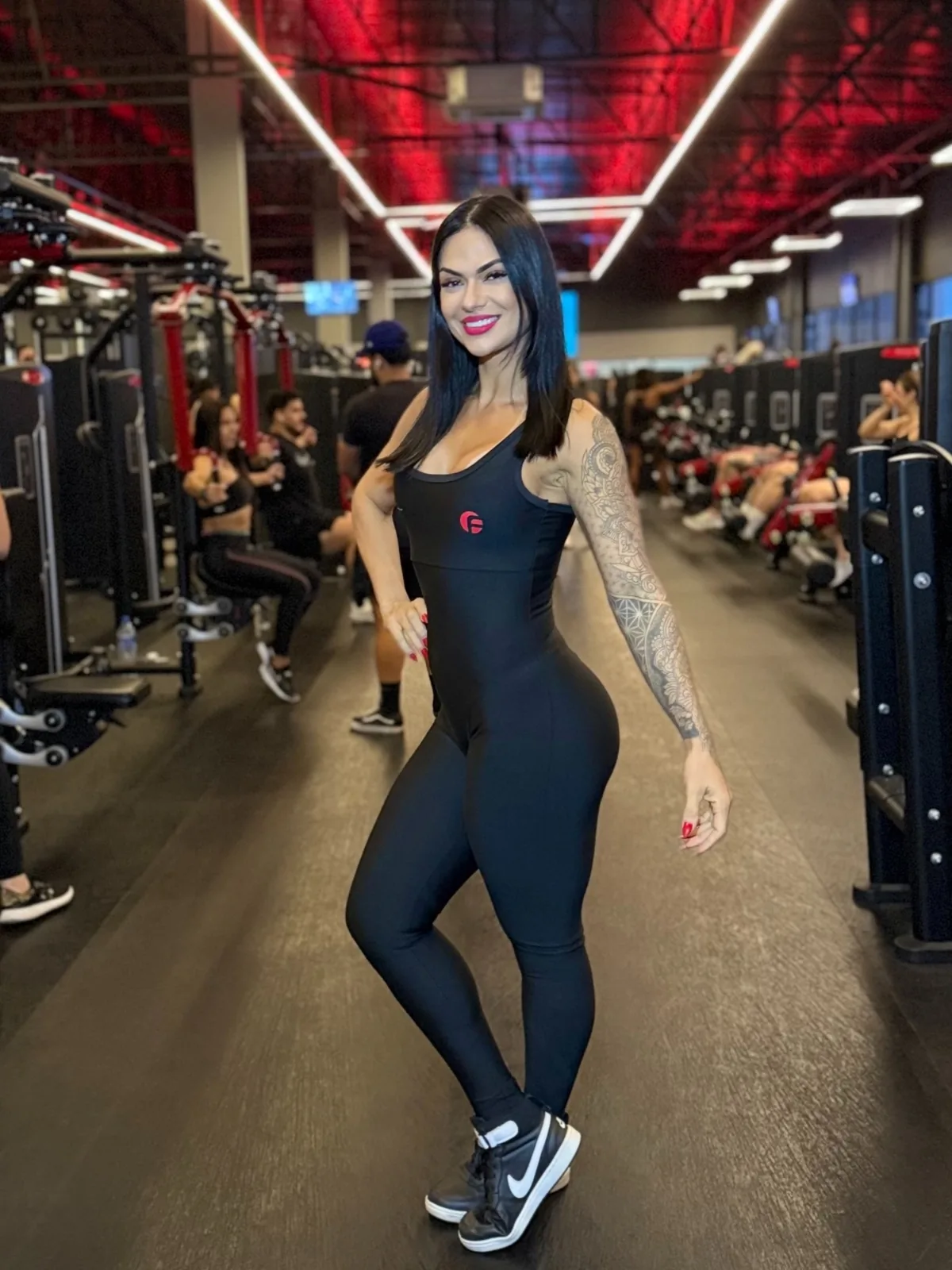 Beatriz Faria de macacão preto em um corredor de academia de grande porte